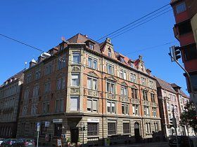 An einer Straßenecke steht ein großes Backsteingebäude mit vielen Fenstern.