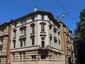 An einer Straßenecke steht ein großes Gebäude mit vielen Fenstern.