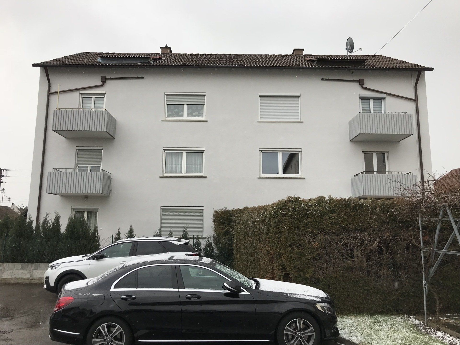 Ein schwarzes Auto parkt vor einem weißen Gebäude.