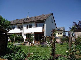 Ein großes weißes Haus mit einem üppig grünen Garten davor.