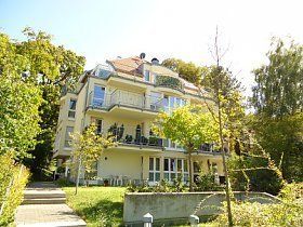 Ein großes Gebäude mit vielen Fenstern und Balkonen ist von Bäumen umgeben.