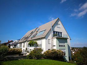 Auf einem grasbewachsenen Hügel steht ein großes weißes Haus.