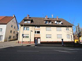An einer Straßenecke steht ein großes weißes Gebäude mit einem braunen Dach.