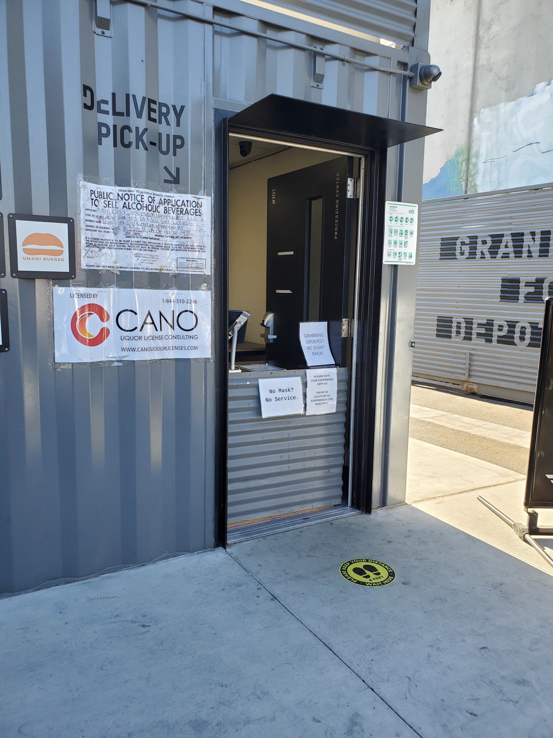 Delivery pickup window in a grey container, with signage and a social distancing sticker.