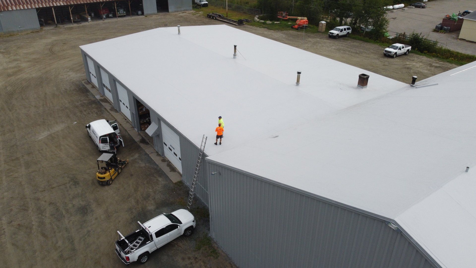 Aerial view of a large metal-roofed building with Rodd Roofing signage and a worker on top.
