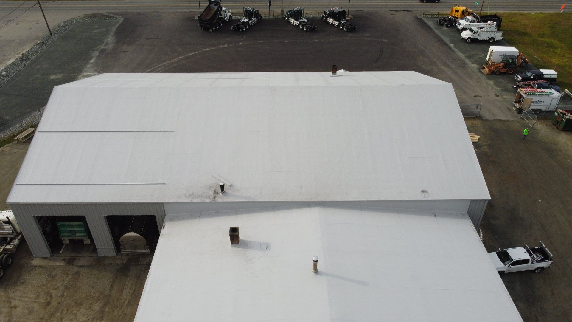 Aerial view of Rodd Roofing’s metal retrofit project, showcasing a large white roof with vents and vehicles below.