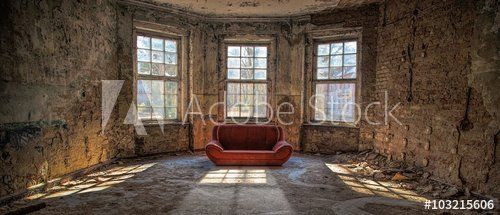 Ein alter, heruntergekommener Raum mit einem roten Sofa in der Mitte vor drei Fenstern.
