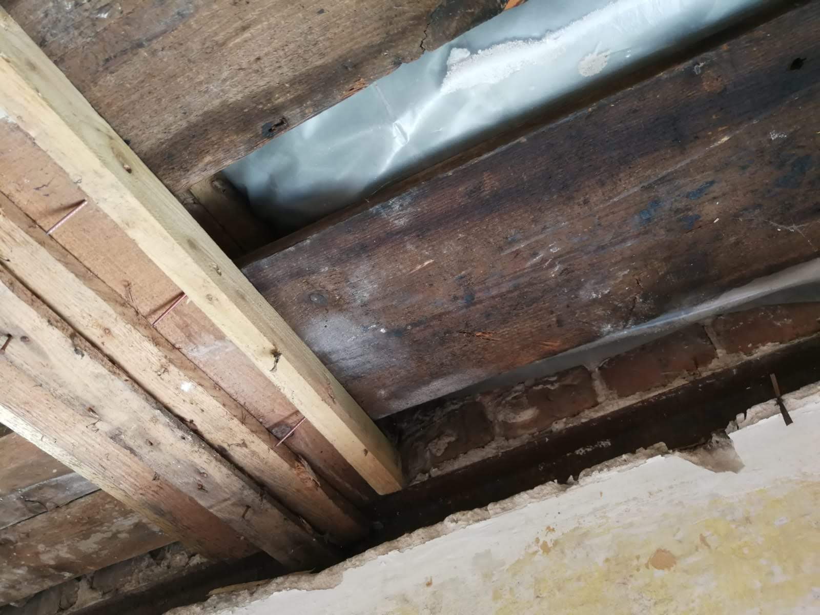 Holzbalken an der Decke mit Sichtziegeln und einer Schicht Plastikfolie.