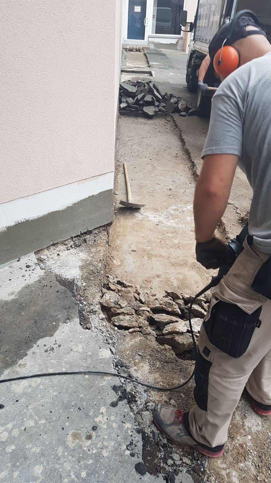 Bauarbeiter bricht mit Presslufthammer Beton an der Seite eines Gebäudes auf.
