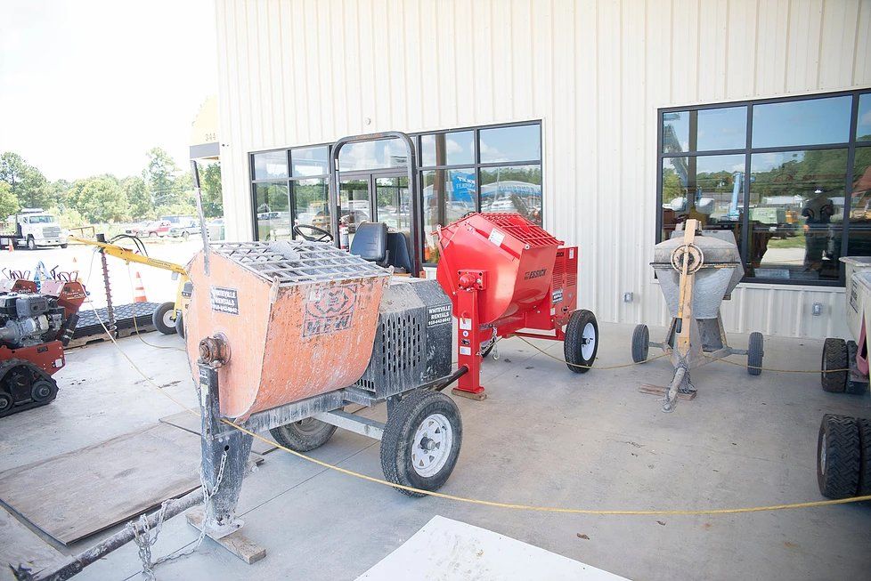 Cement mixers on display outside a store with large windows. One is orange, another red.