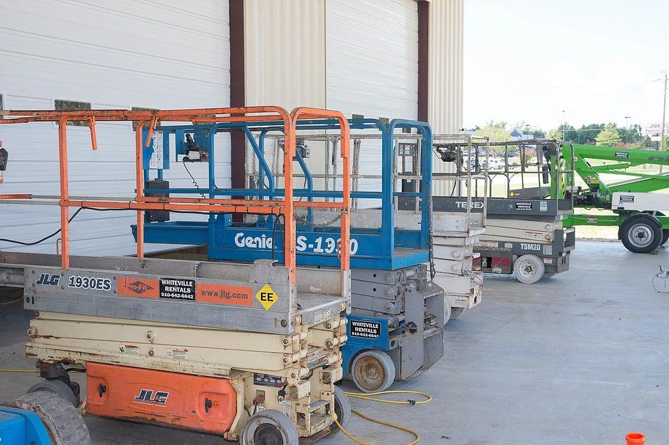 Several parked scissor lifts, mostly blue and orange, in an open-air building.