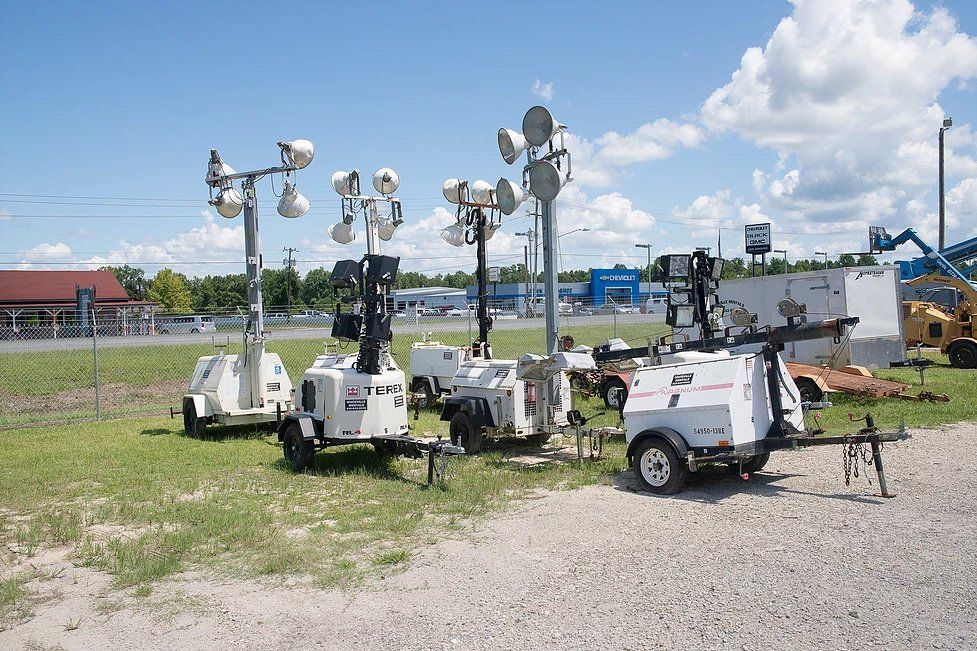 Several mobile light towers on a grassy area, under a blue sky with clouds.