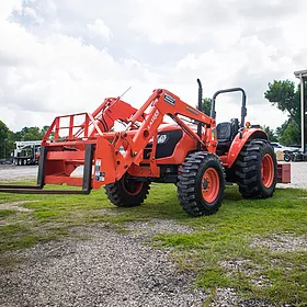Orange tractor with a front loader and forks on grass.