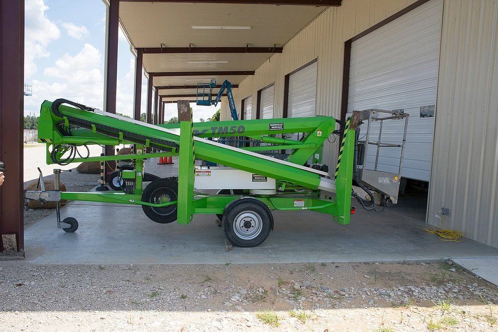 Green lift equipment on a trailer parked outside a building with loading bay doors.