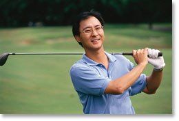 Golfer in a blue polo smiling mid-swing on a green golf course
