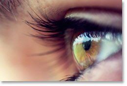 Close-up of a human eye with long eyelashes and a green-gold iris in soft light