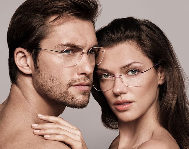 Two people wearing glasses pose closely together against a neutral background.