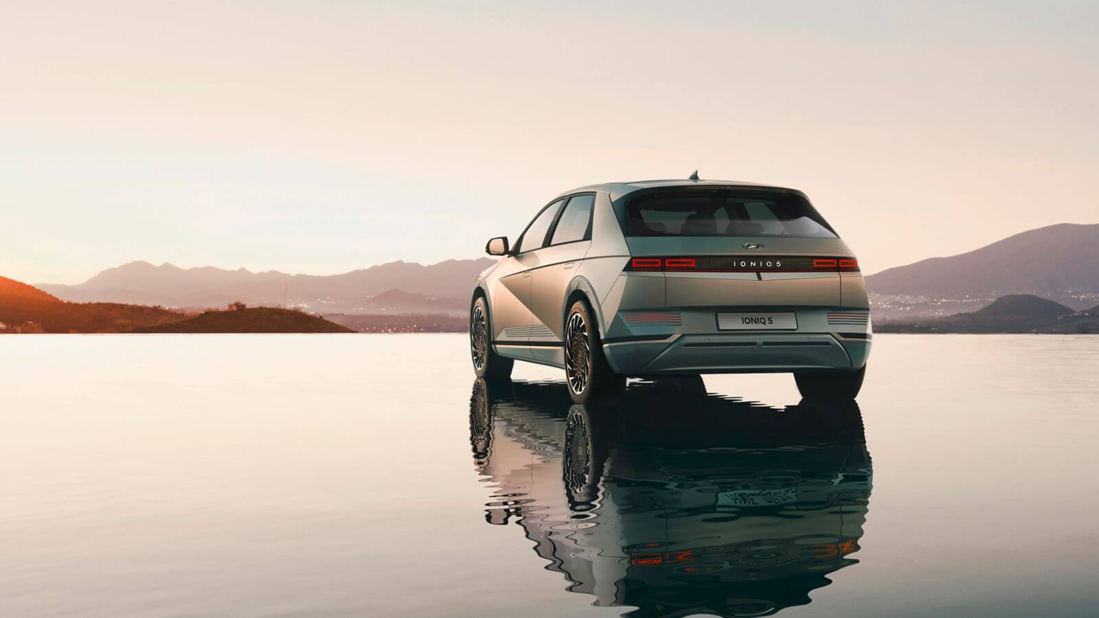 A car is parked in the middle of a lake with mountains in the background.  ioniq 5 
