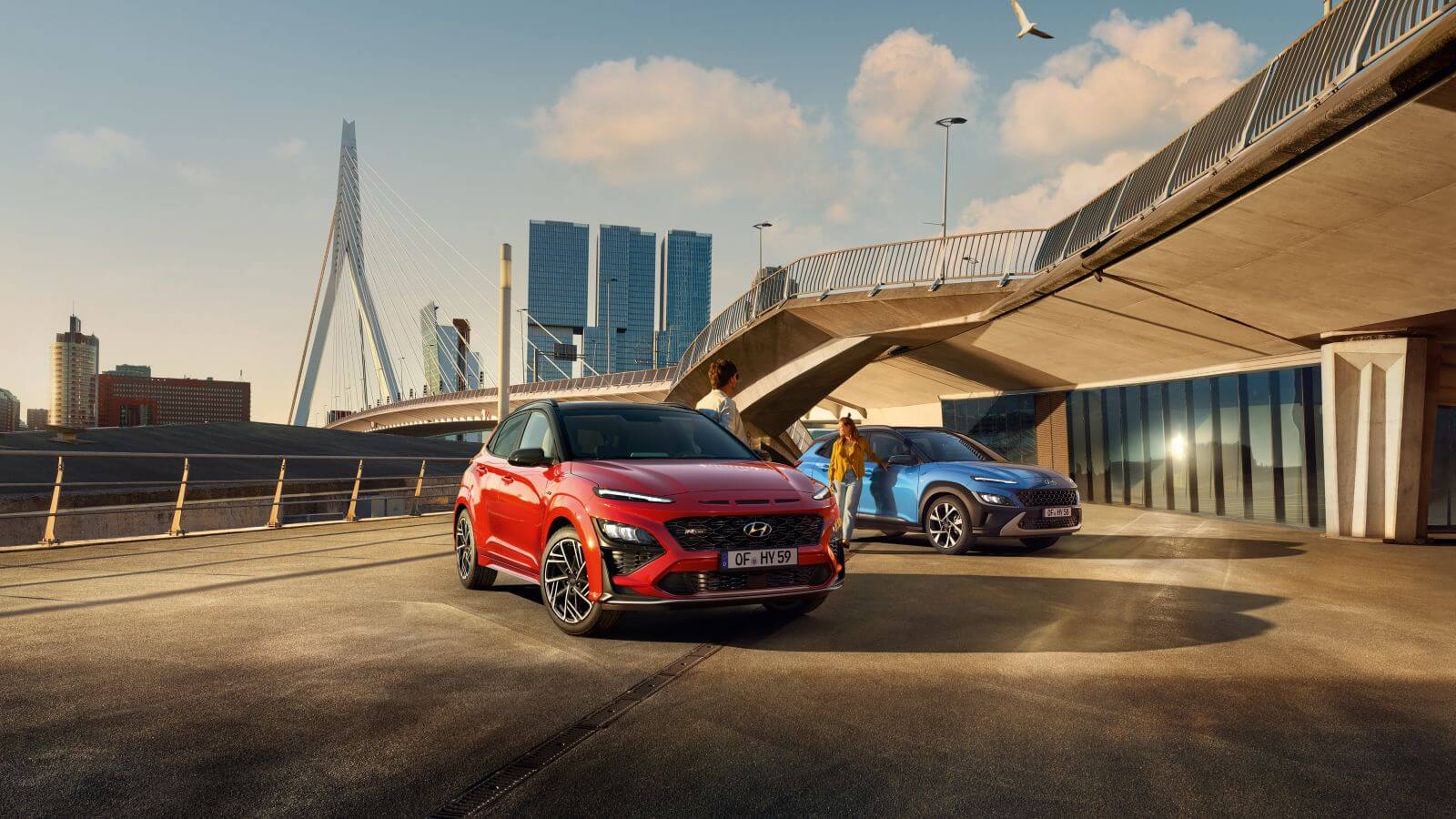 Two cars are parked under a bridge in front of a building.