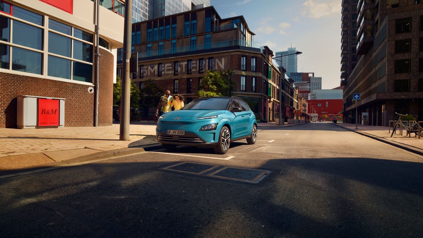 A blue car is driving down a city street.