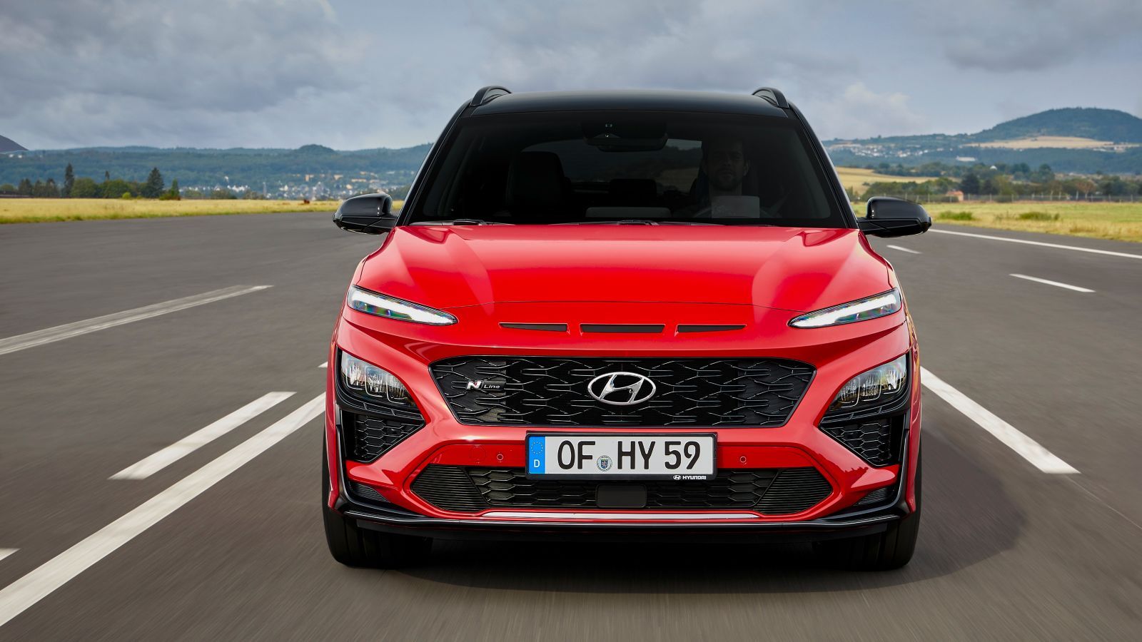 A red hyundai kona is driving down a road.