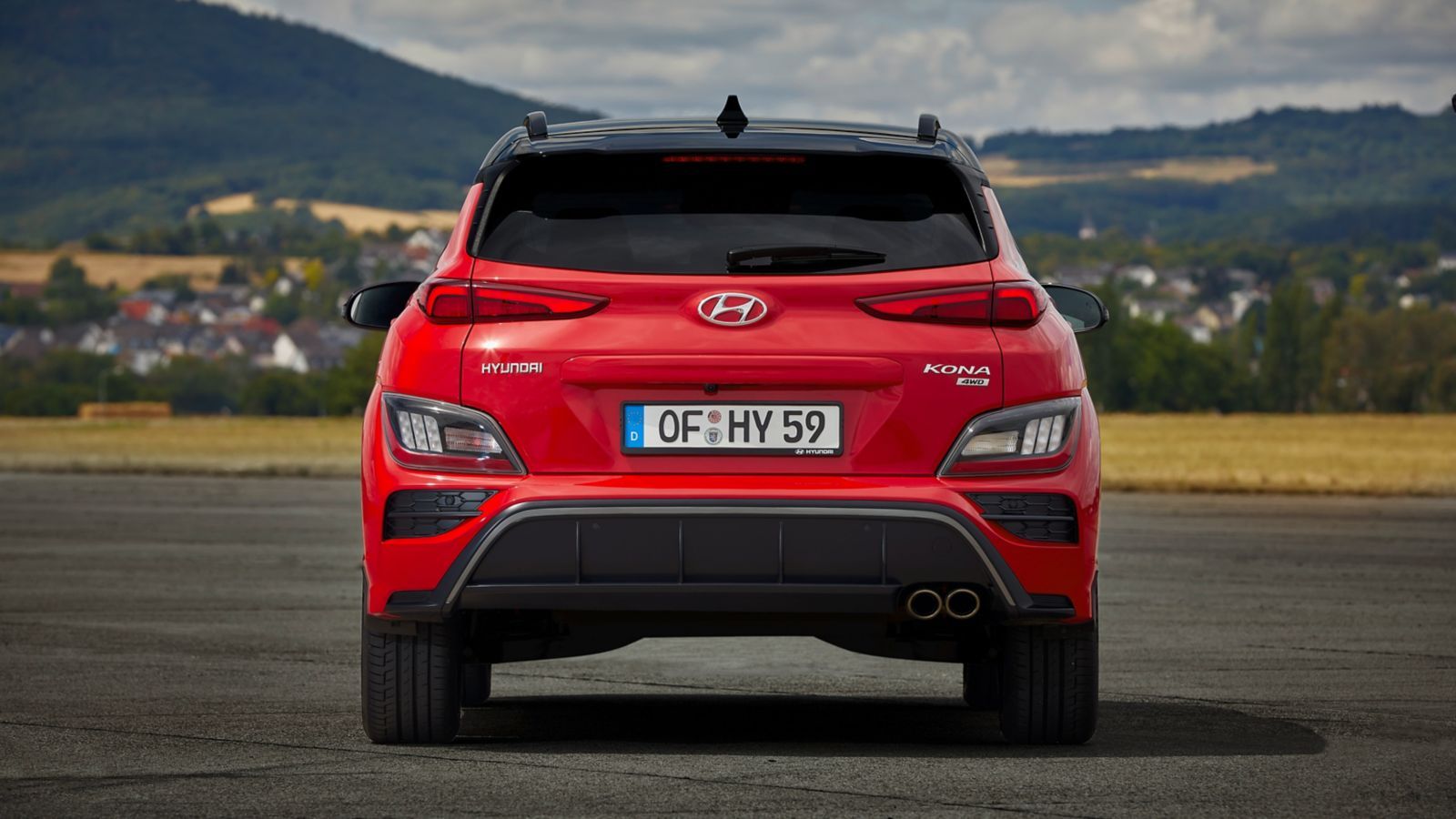 The rear end of a red hyundai kona is parked on a road.