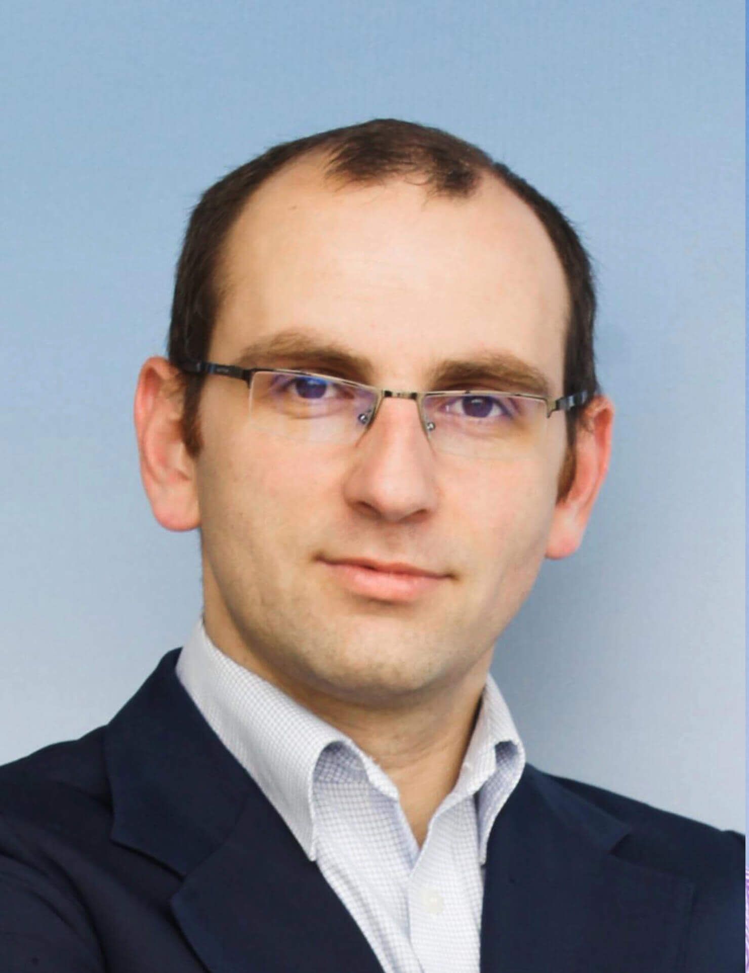 A man wearing glasses and a suit looks at the camera