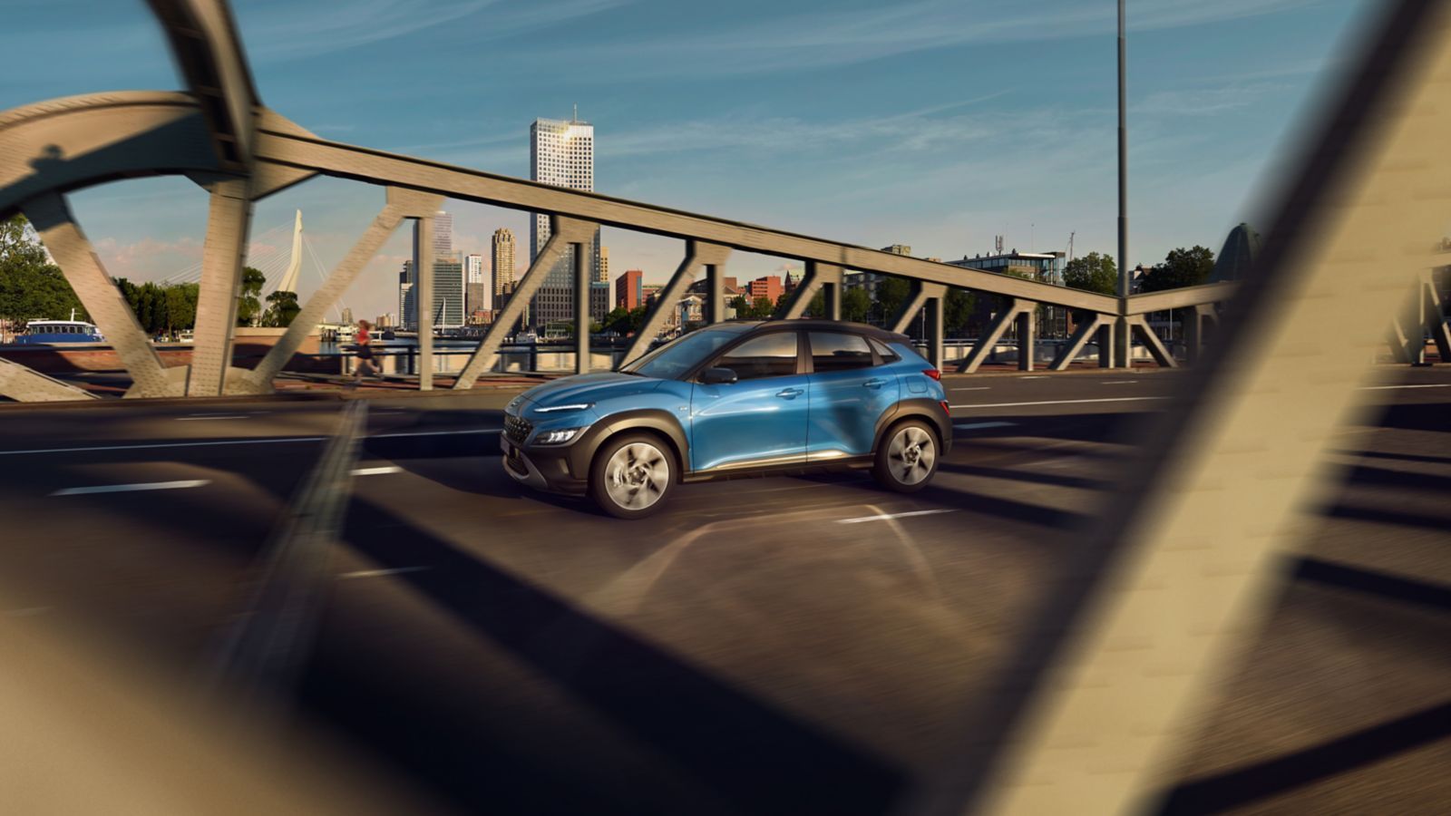 A blue car is driving down a highway under a bridge.