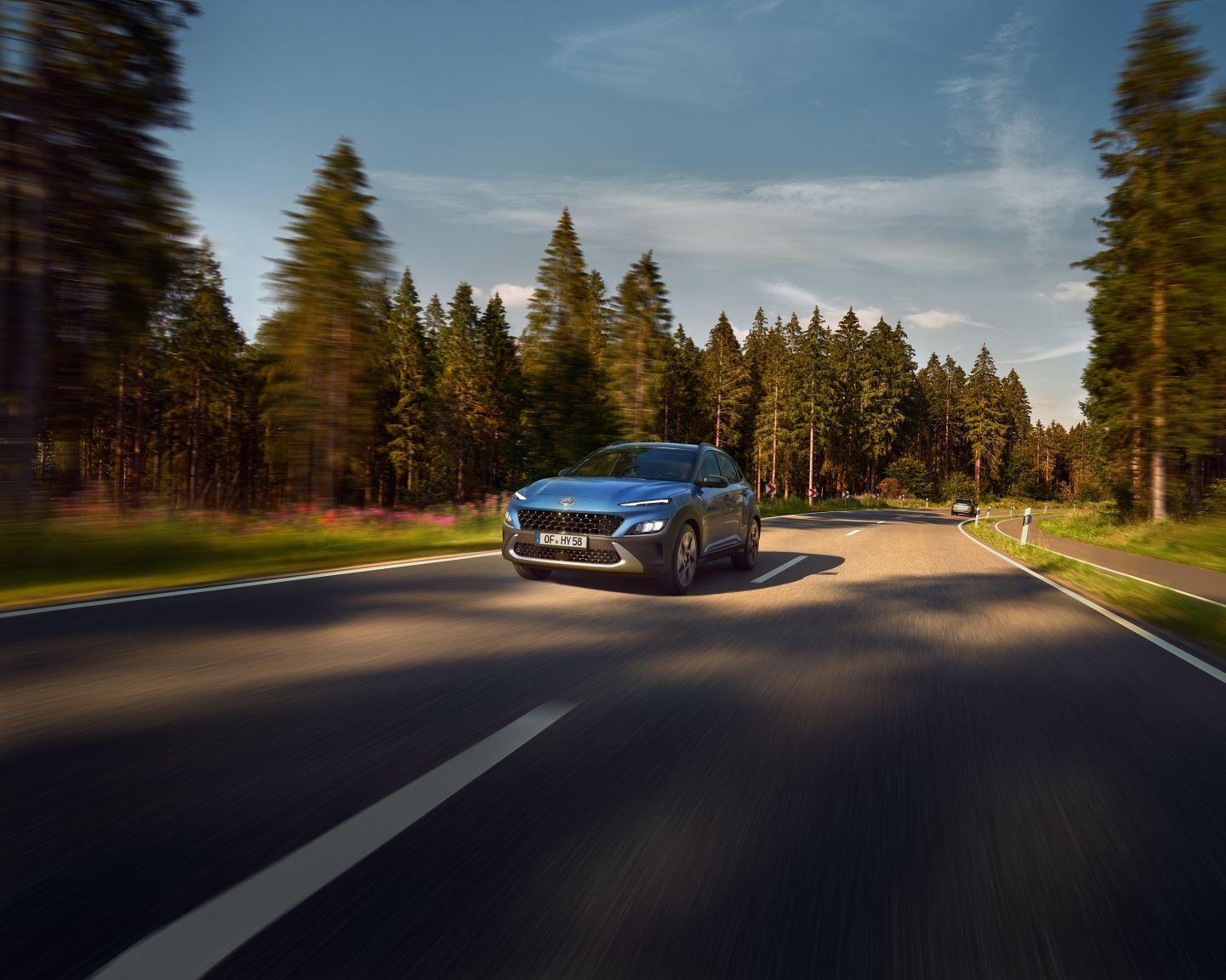 A blue car is driving down a road next to a forest.
