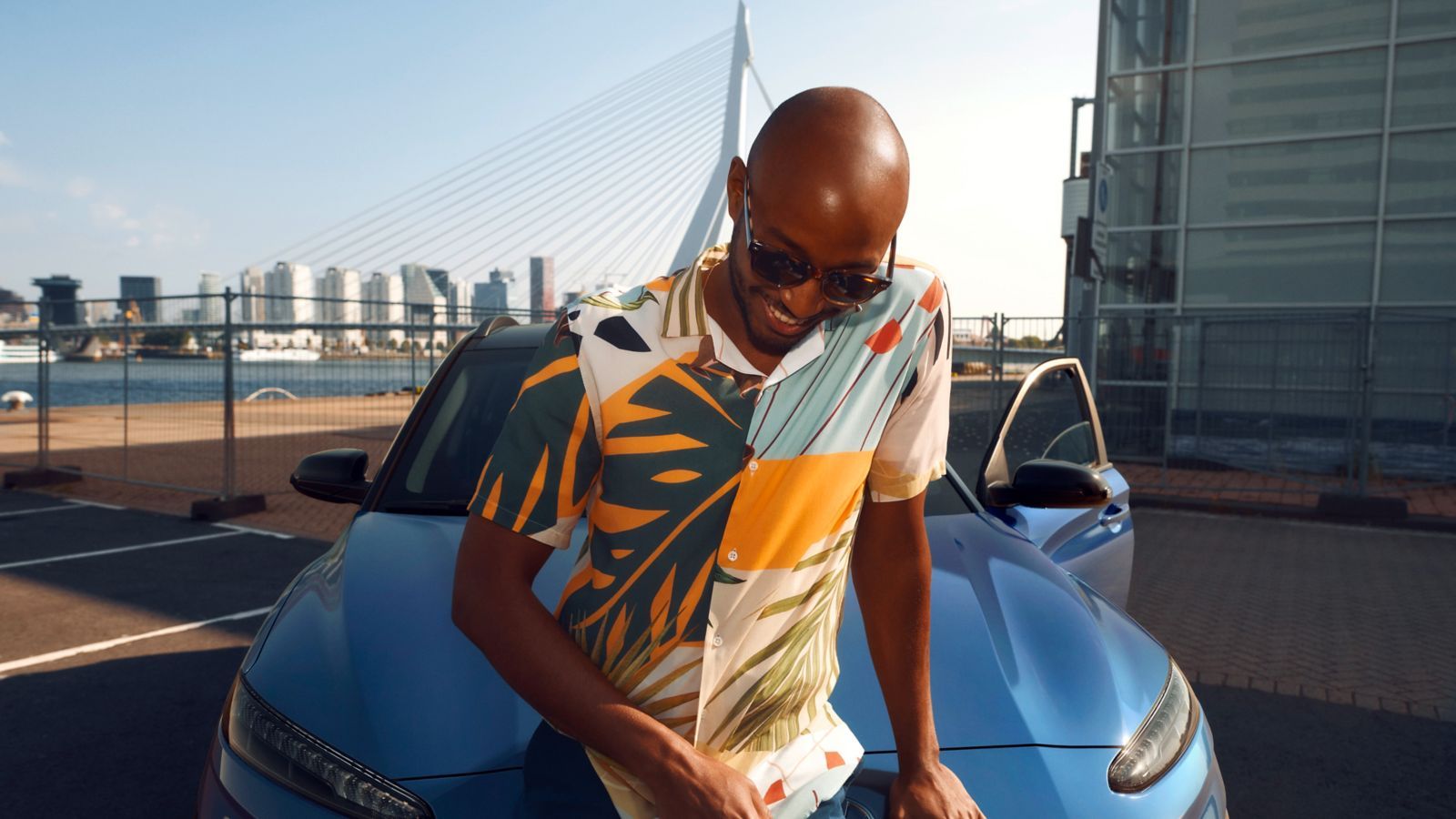 A man is sitting on the hood of a blue car.
