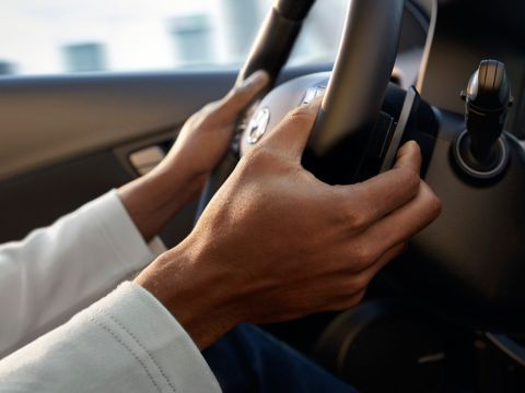 A person is driving a car with their hands on the steering wheel. Kona Hibrid