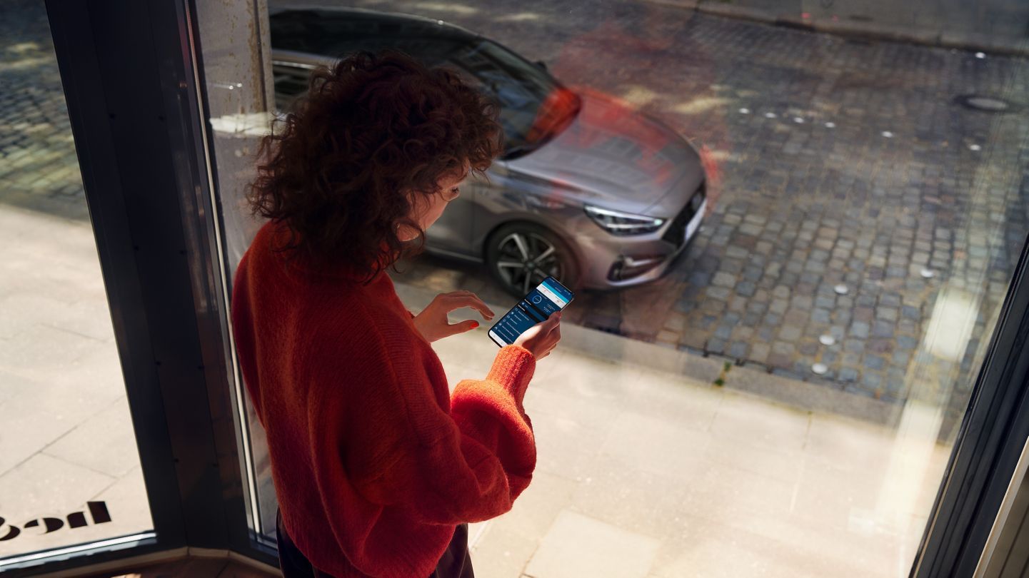 A woman is standing in front of a window looking at her phone.