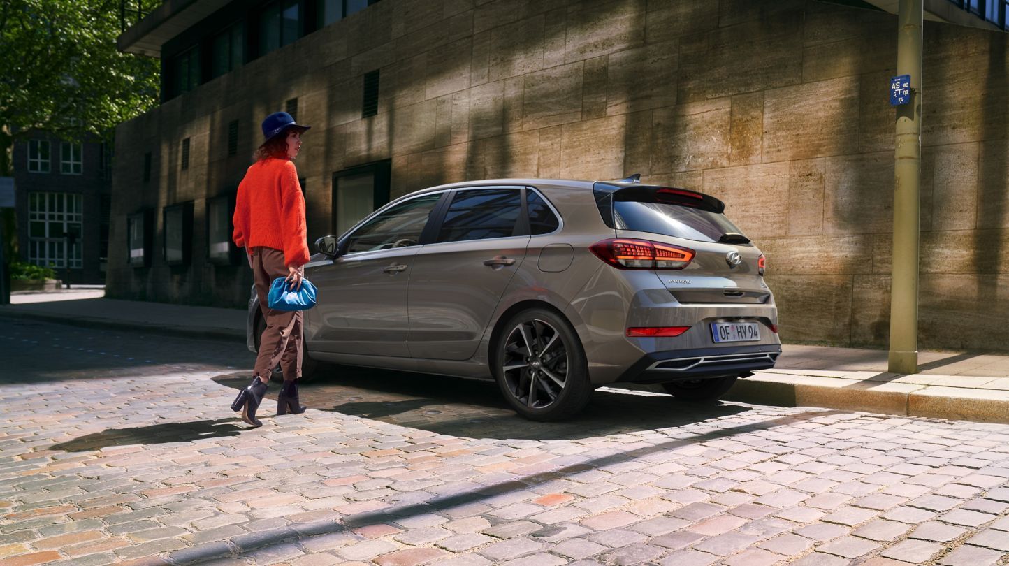 A woman is walking down a cobblestone street next to a parked car.