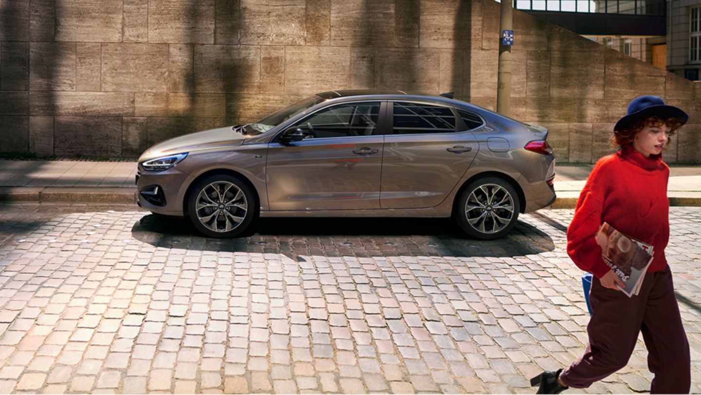 A woman is walking down a cobblestone street next to a car.