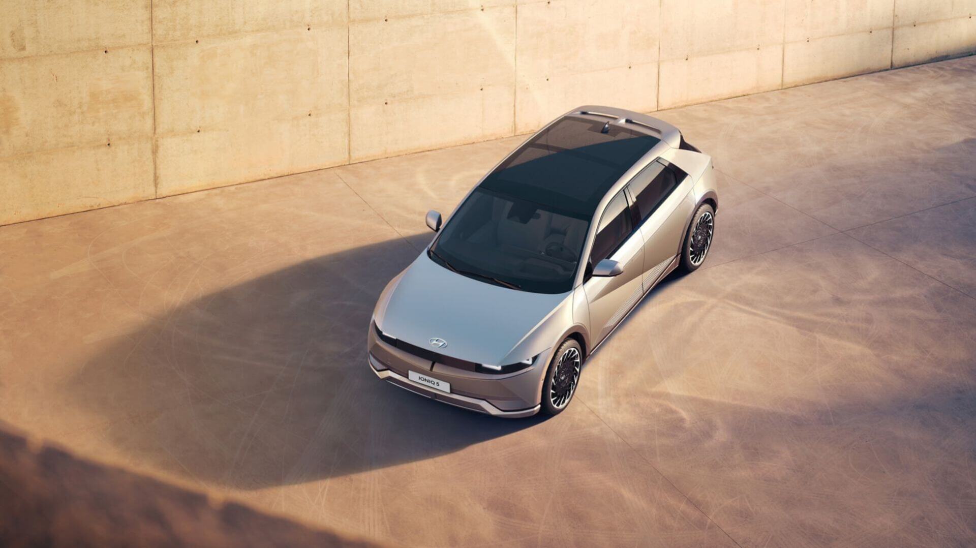 A silver car is parked in a parking lot next to a wall.