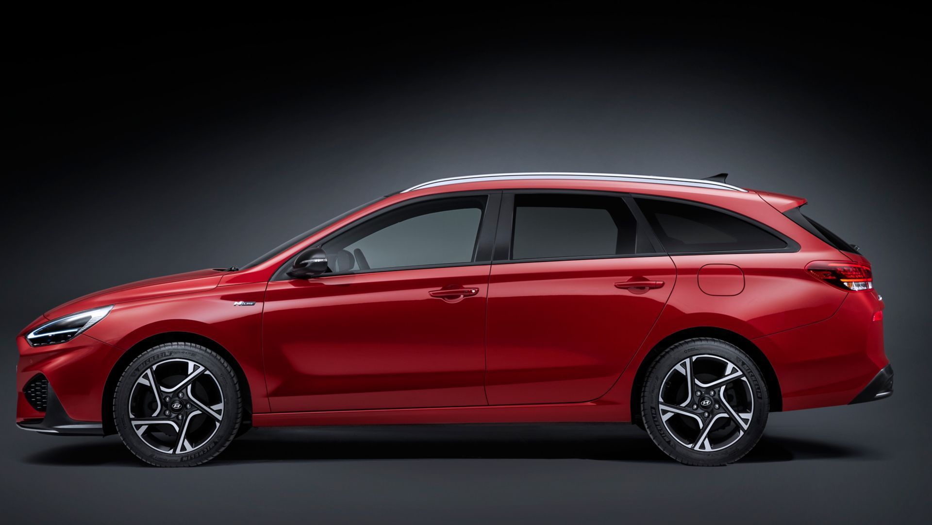 A red station wagon is parked on a black background.