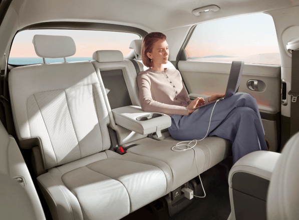 A woman is sitting in the back seat of a car using a laptop.  ioniq 5 