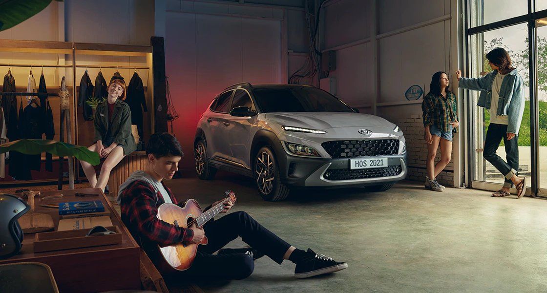 A man is playing a guitar in front of a car in a garage.