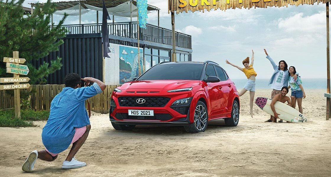 A man is taking a picture of a red car on the beach.