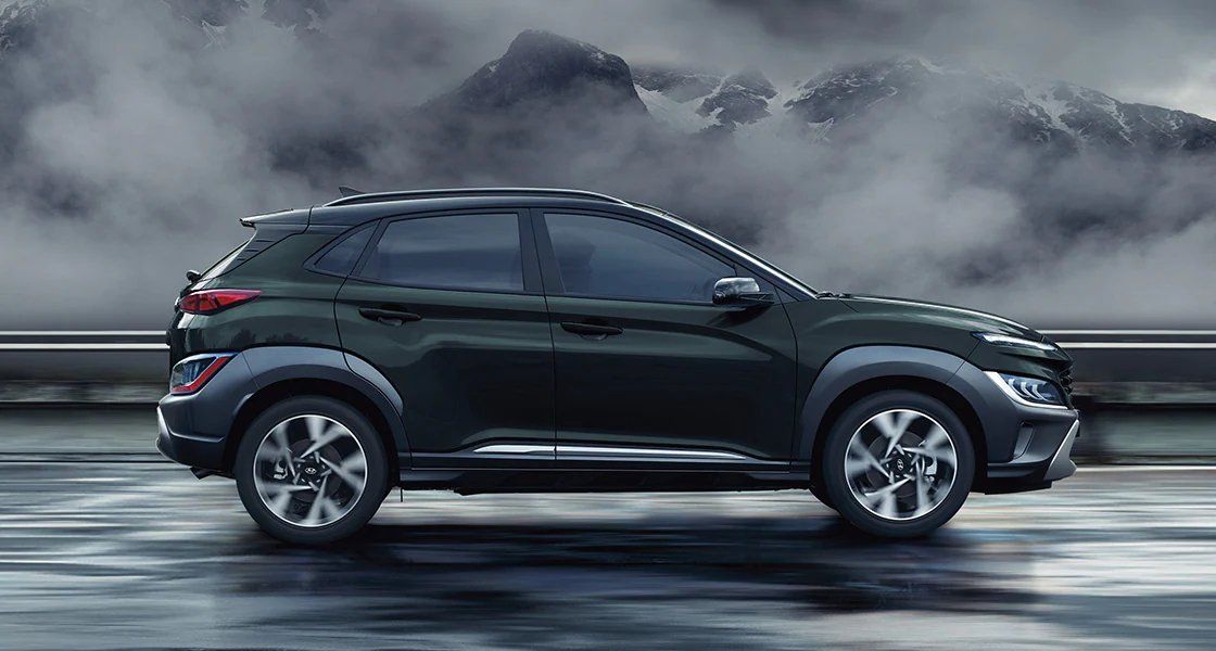 A black suv is driving down a wet road with mountains in the background.