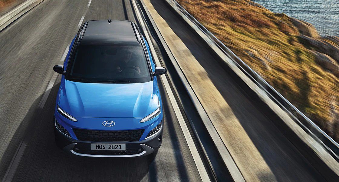 A blue car is driving down a road next to a body of water.