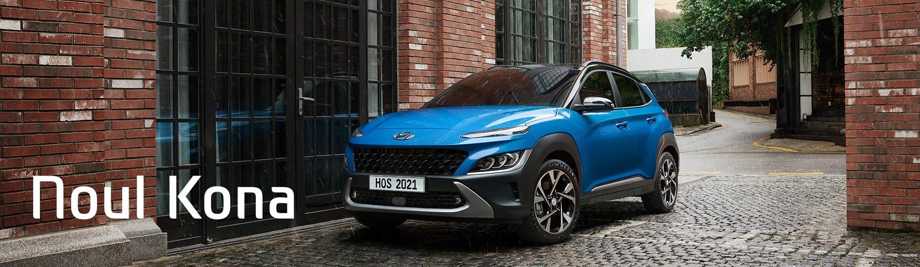 A blue hyundai kona is parked in front of a brick building.