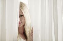 Woman looking through clean, white drapes