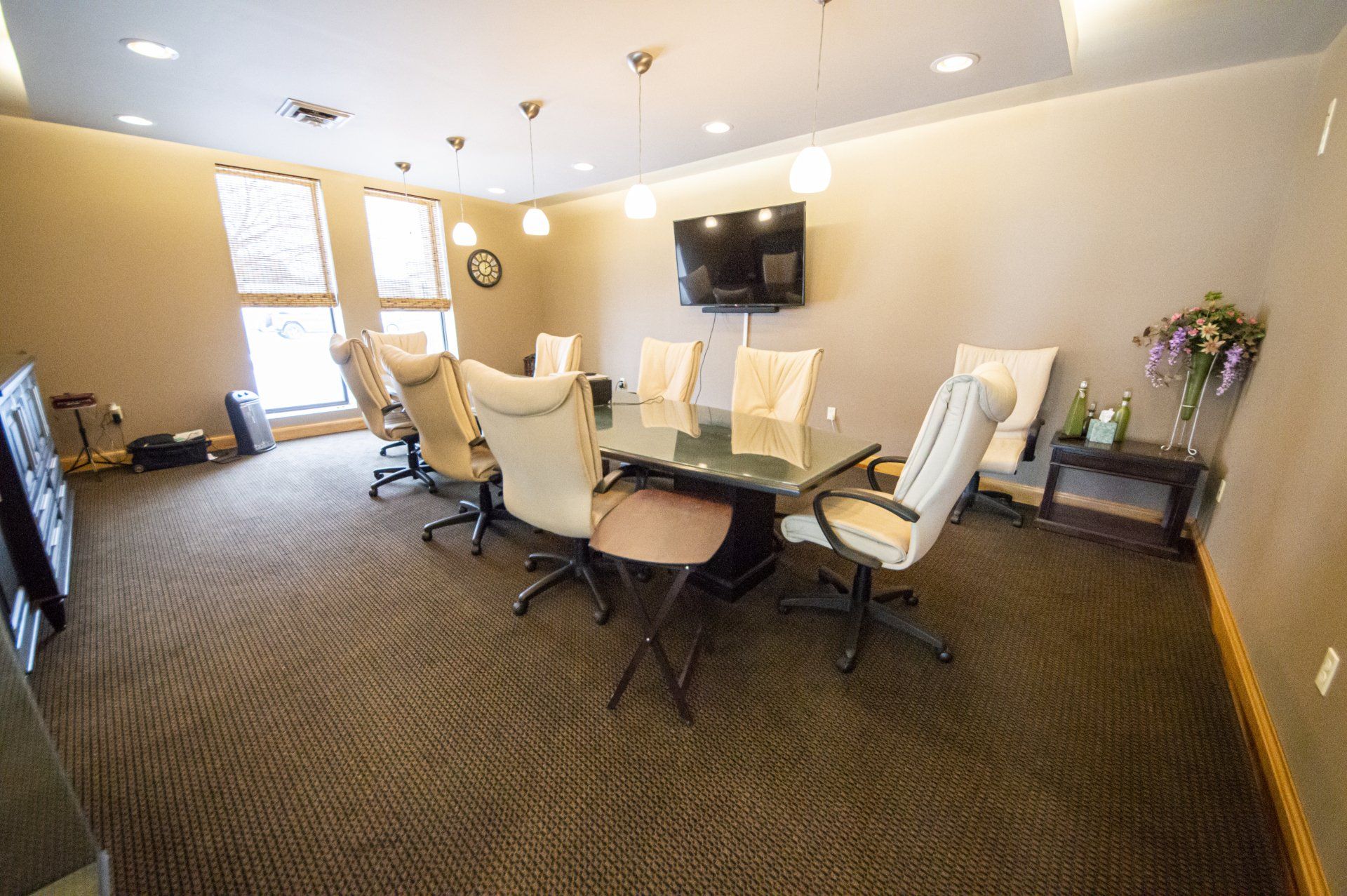 Conference room with a rectangular glass table, cream leather chairs, and a mounted TV.