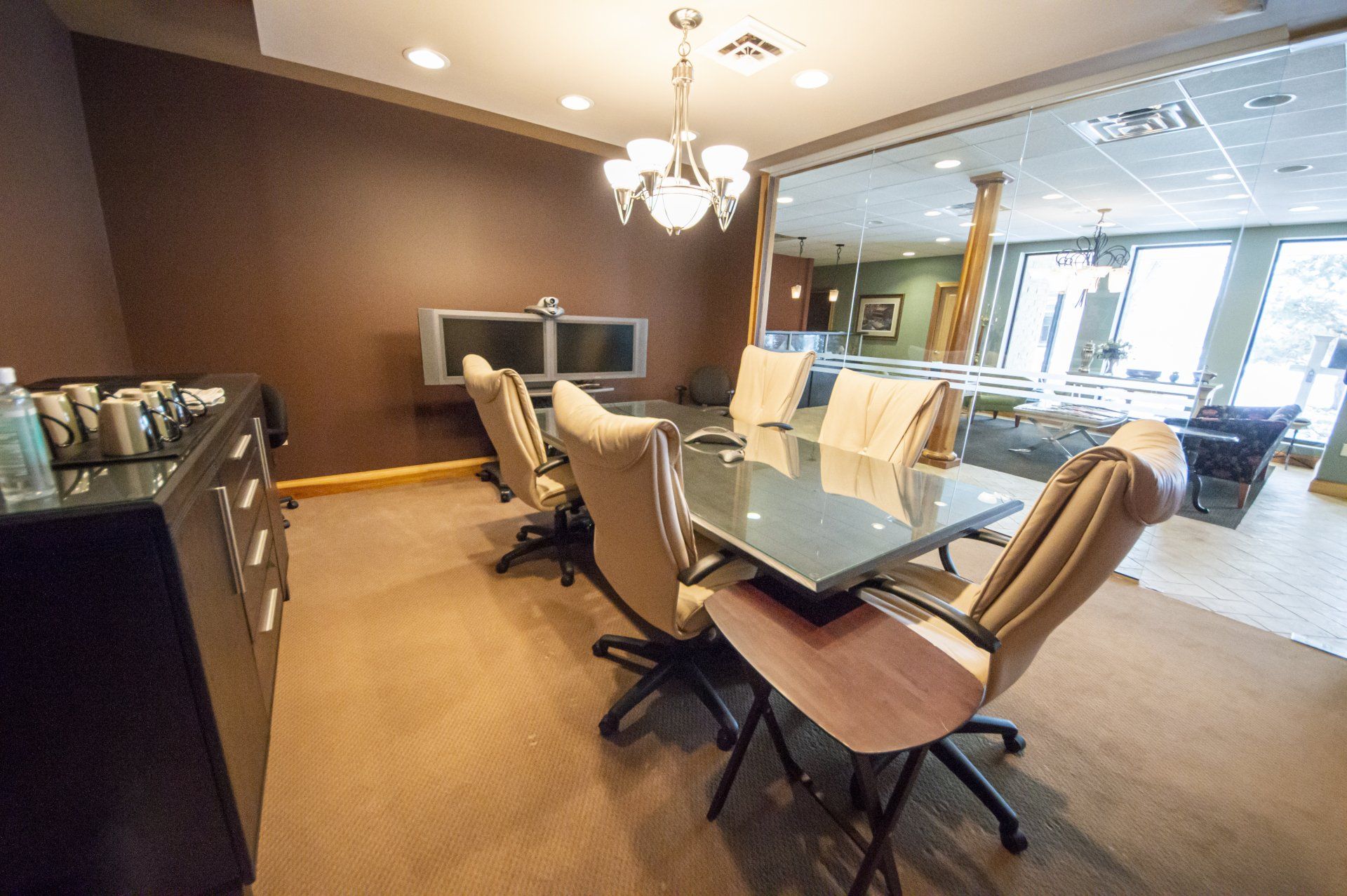 Conference room with table, chairs, TV monitors, and buffet. Brown walls, beige carpet, and glass door.