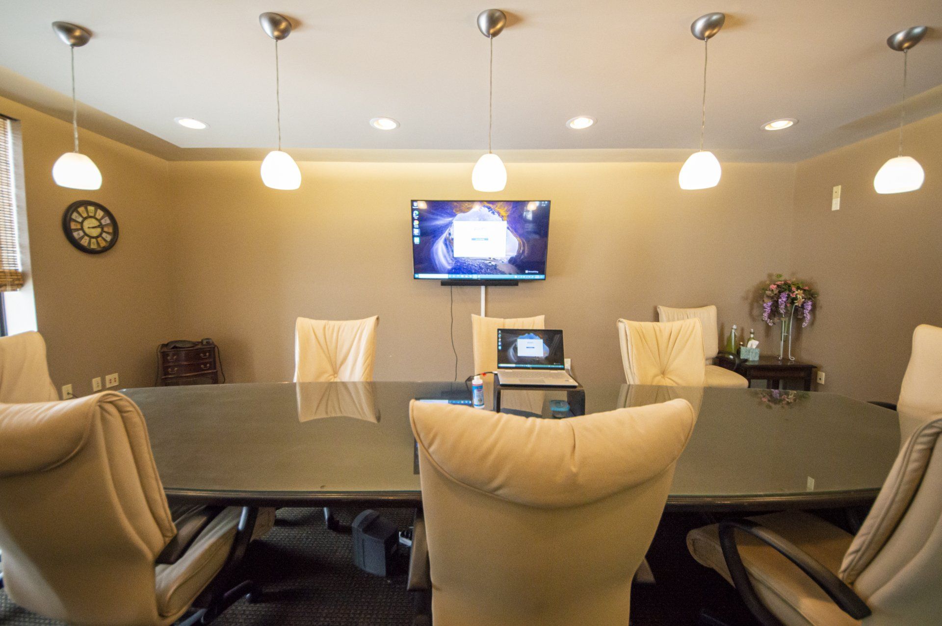 A conference room with a large table, chairs, TV, and pendant lights.