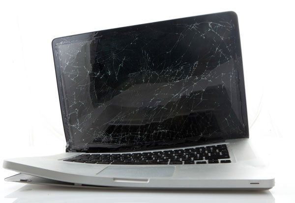 A laptop with a broken screen is laying on its side on a white surface.