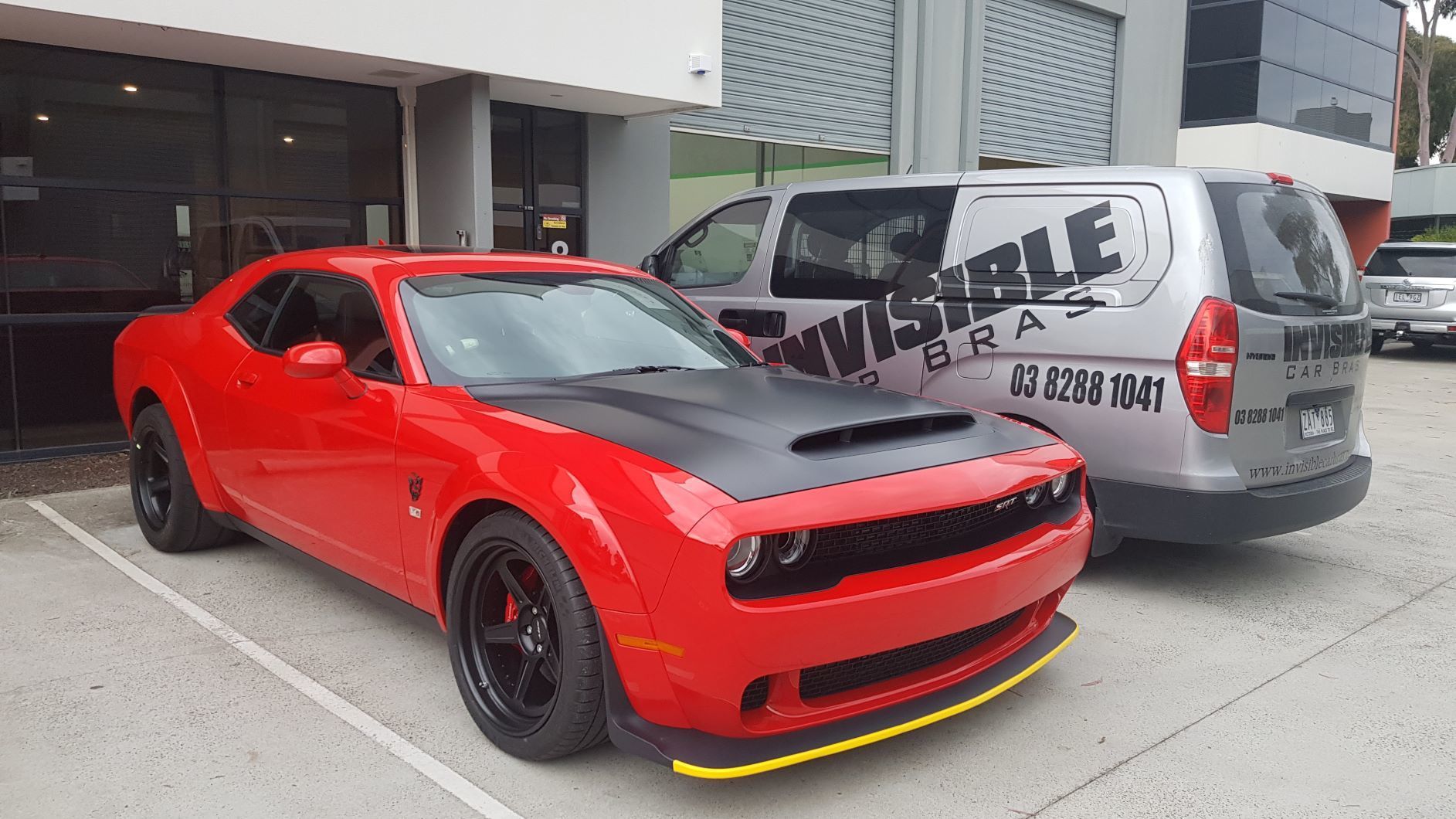 red Dodge Challenger SRT Demon parked in a lot with a silver van