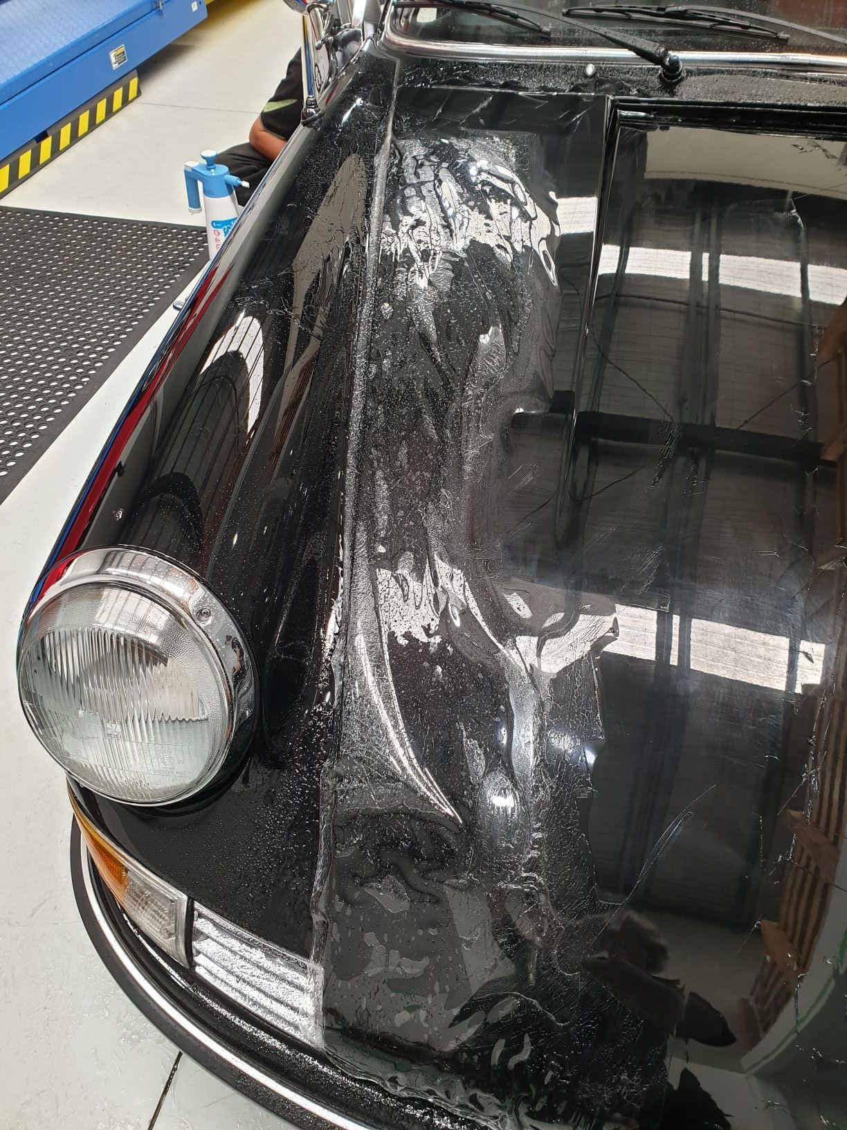 image shows the front of a black Porsche 911, undergoing restoration or paint correction