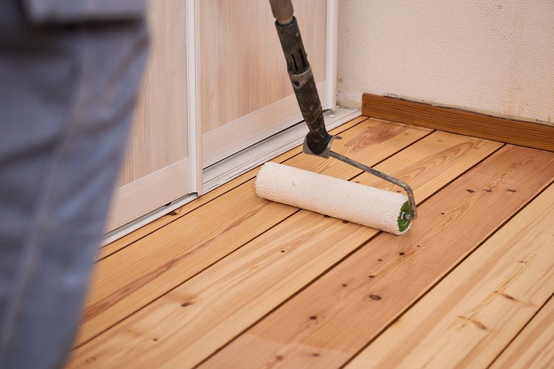 En person bruker en malerrulle til å påføre en klar overflate eller beis på ubehandlede tregulvplanker.
